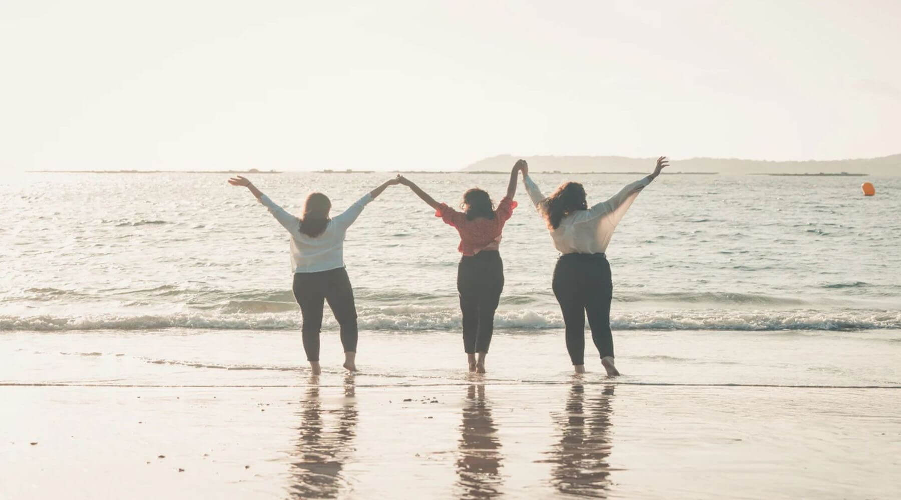 Three women 3 hold hands with their arms to the sky