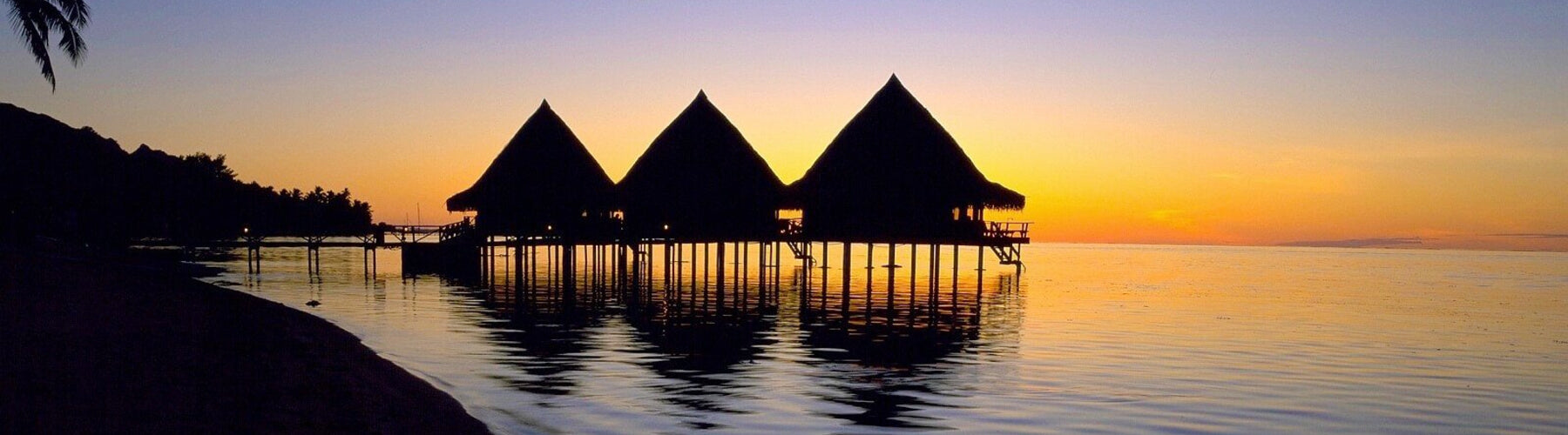 Three vacation lodges on stilts over the sea at sunset