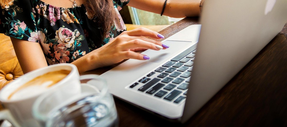 Lady typing on a laptop computer with a coffee cup